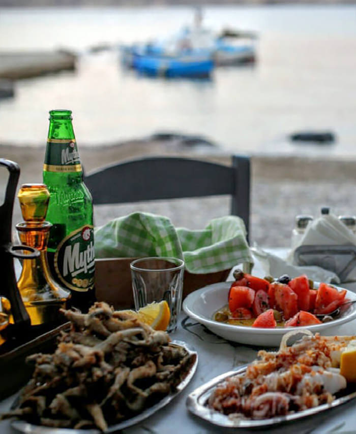 A table with fried fish, calamari, beer and tomato salad by the beach